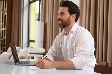 Photo of Man writing something and laptop at table in cafe