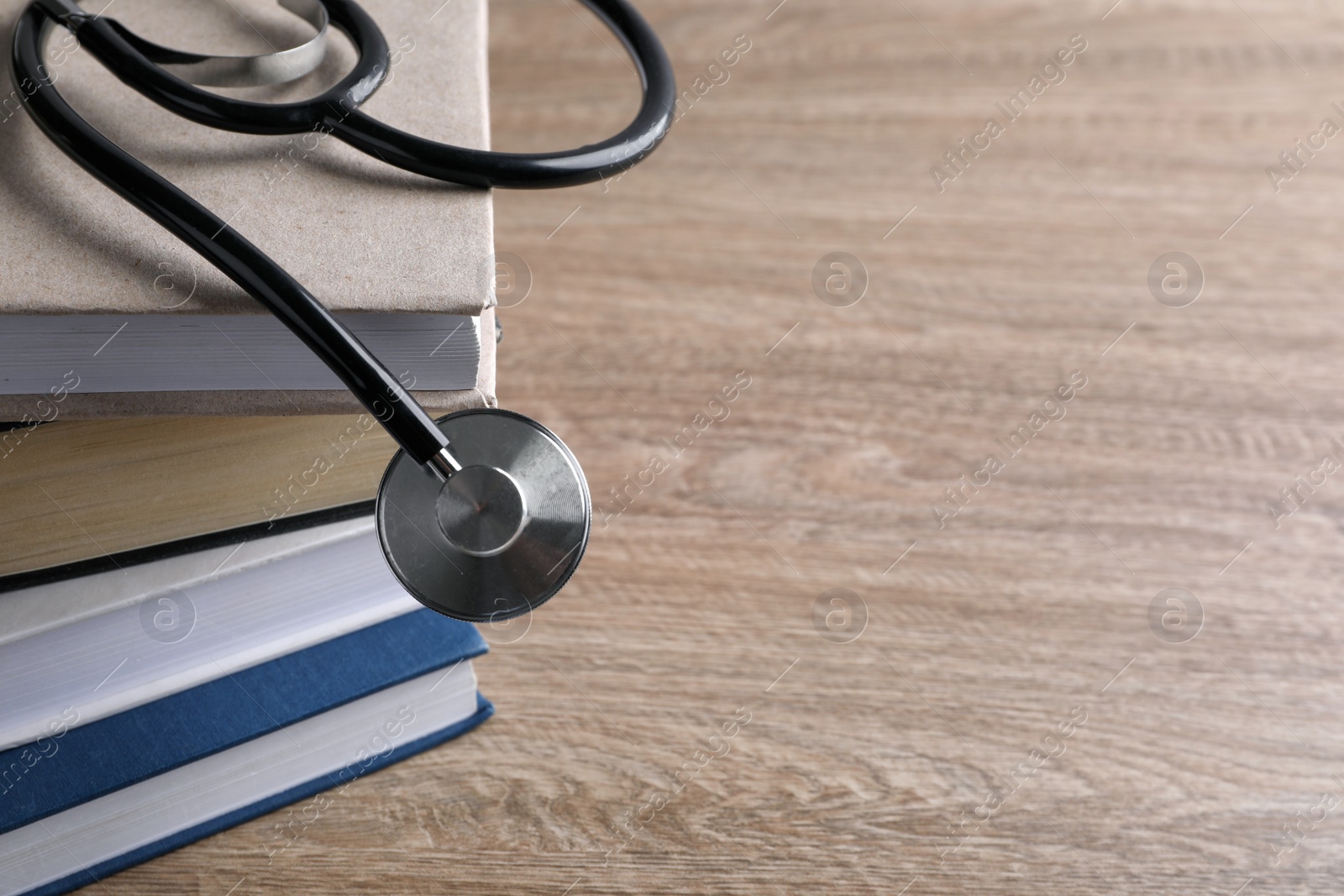 Photo of Stack of student textbooks and stethoscope on wooden table, closeup view with space for text. Medical education