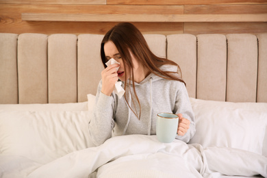 Sick young woman with cup of hot drink in bed at home. Influenza virus