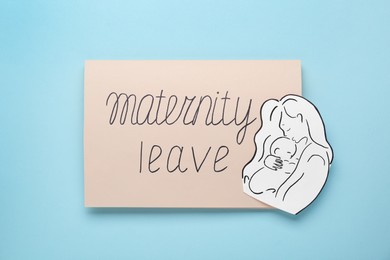 Photo of Card with phrase Maternity Leave, paper cutout of mother and child on light turquoise background, top view