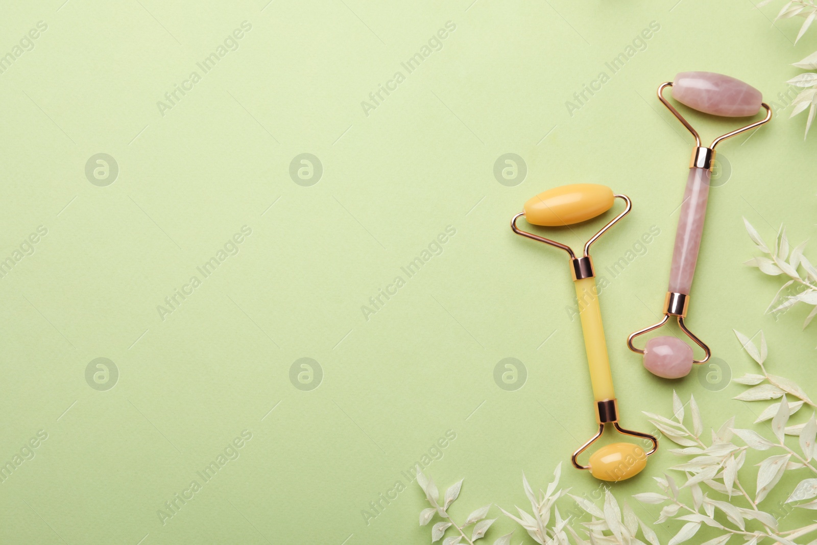 Photo of Natural face rollers and leaves on green background, flat lay. Space for text