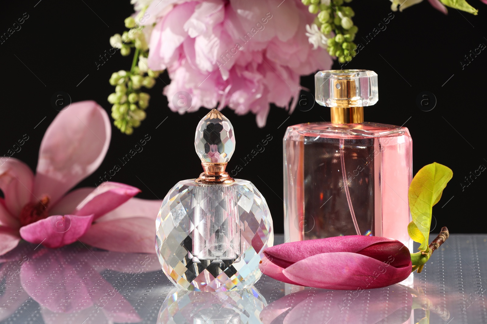 Photo of Luxury perfumes and floral decor on mirror surface against black background