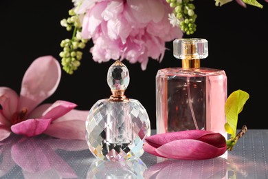 Luxury perfumes and floral decor on mirror surface against black background