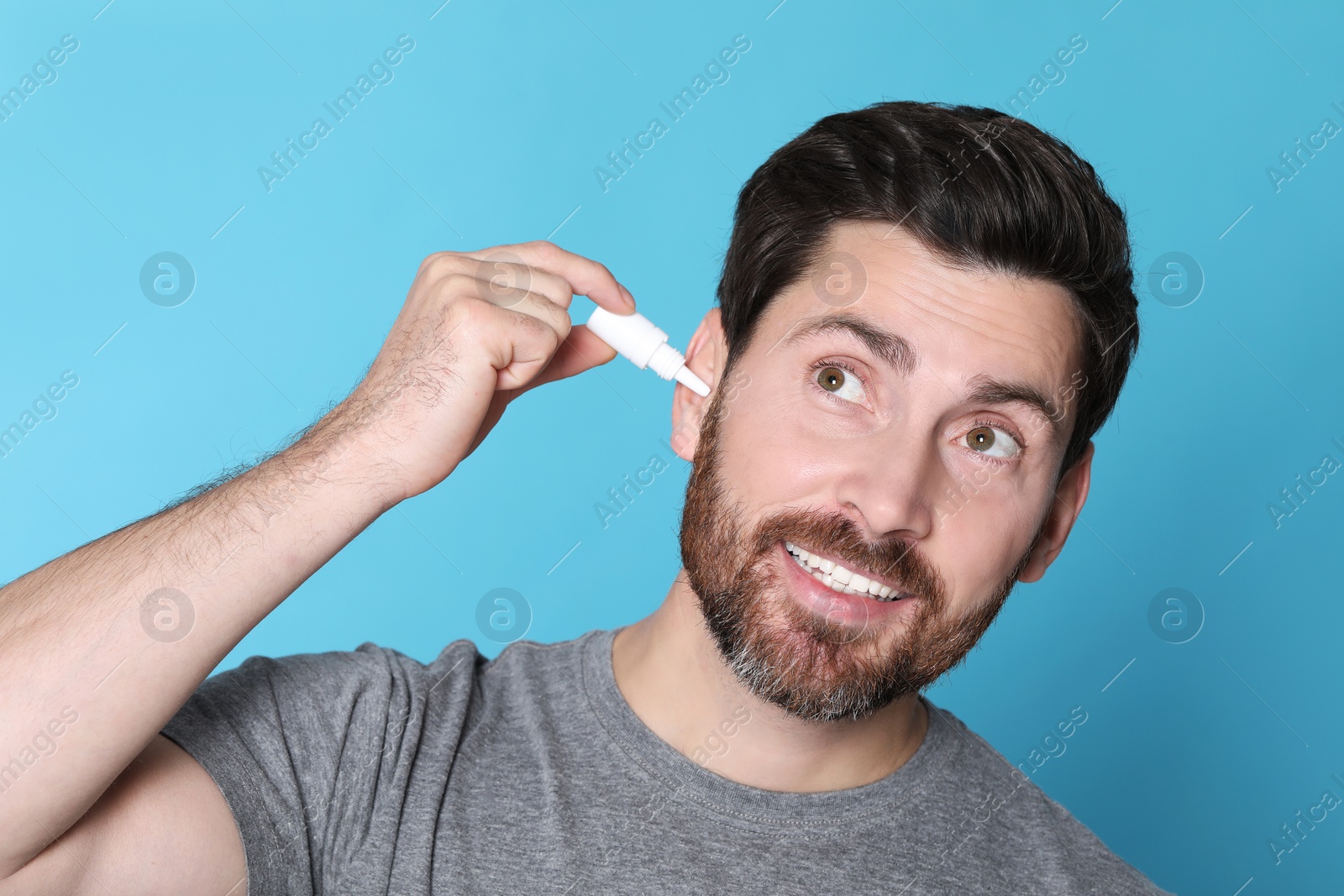 Photo of Man using ear drops on light blue background