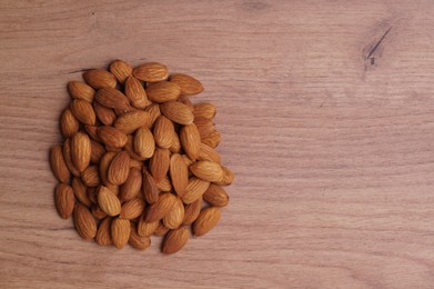 Photo of Pile of delicious almonds on wooden table, top view. Space for text