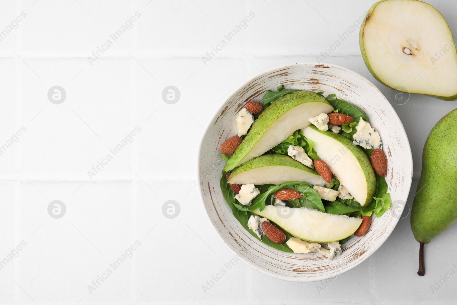 Photo of Delicious pear salad in bowl and fruits on light tiled table, top view. Space for text