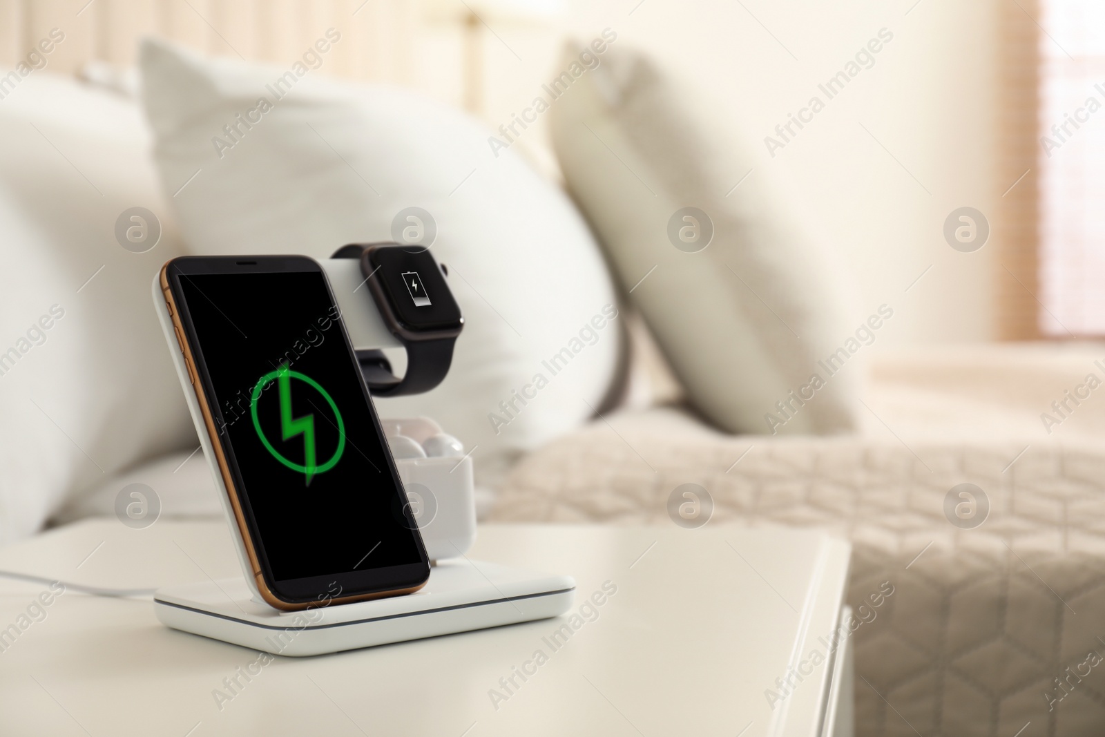 Photo of Different gadgets charging on wireless pad in bedroom. Space for text