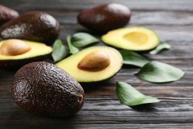 Whole and cut avocados with green leaves on dark wooden table, closeup