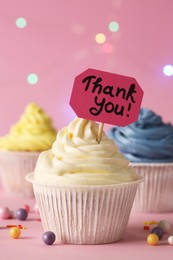 Tasty cupcakes and note with phrase Thank You on pale pink background