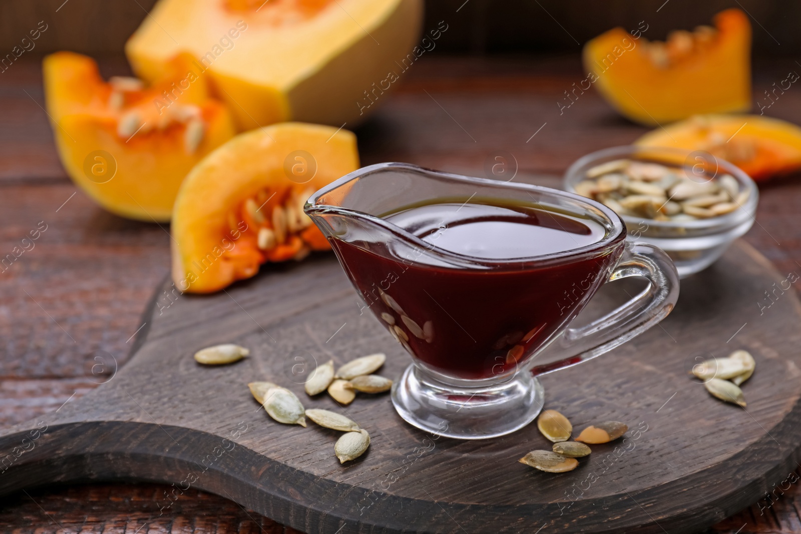 Photo of Fresh pumpkin seed oil in glass sauceboat on wooden table