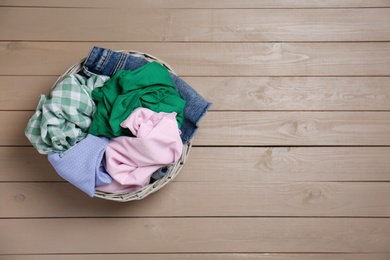 Wicker laundry basket with different clothes on wooden background, top view. Space for text