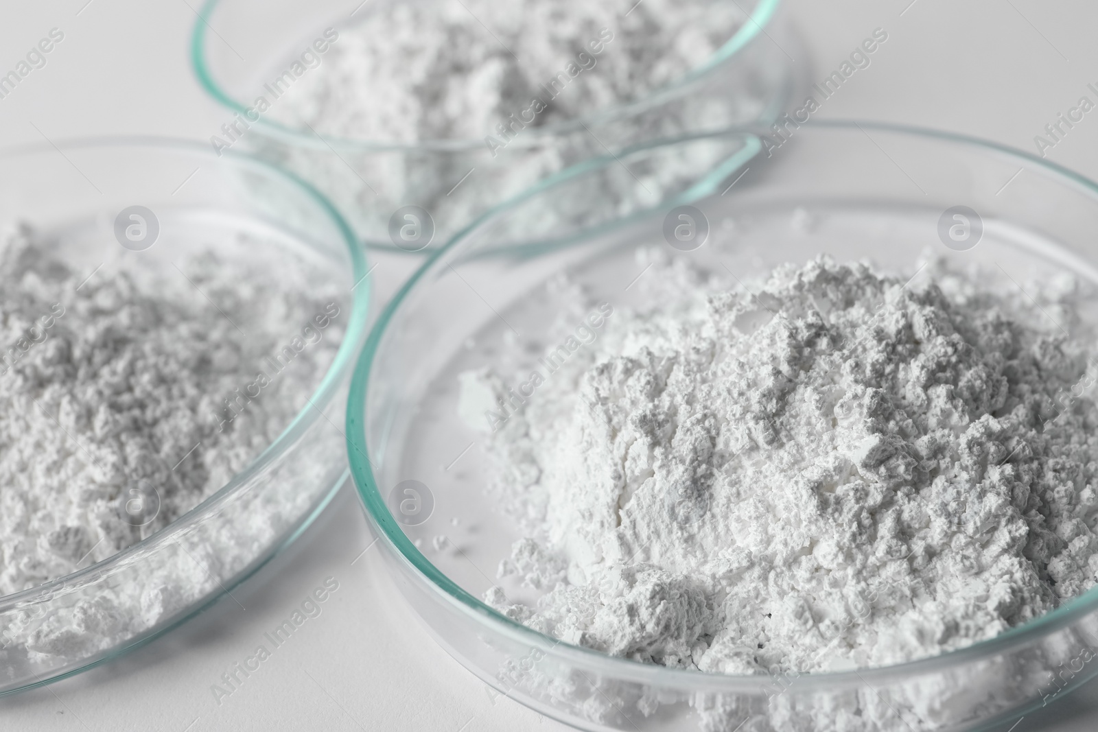 Photo of Petri dishes with calcium carbonate powder on white table, closeup