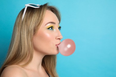 Photo of Fashionable young woman with bright makeup blowing bubblegum on light blue background, space for text