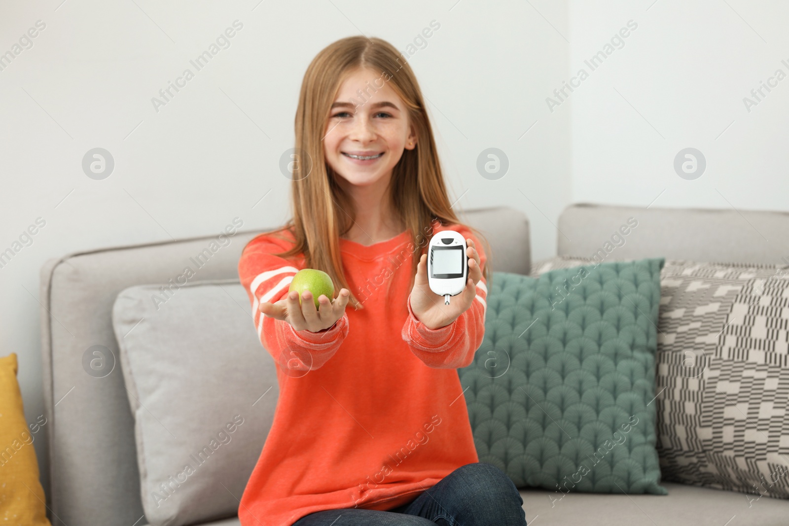 Photo of Teen girl holding digital glucometer and apple at home. Diabetes diet