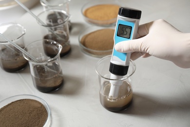 Photo of Scientist measuring acidity and pH of soil at table, closeup. Laboratory analysis