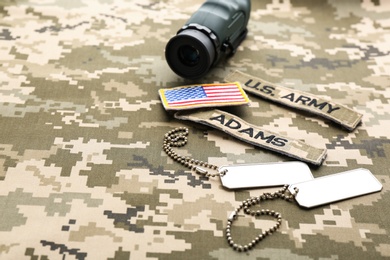 Military ID tags, patches and monocular on camouflage background