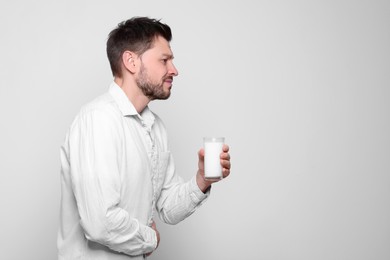 Man with glass of milk suffering from lactose intolerance on white background, space for text