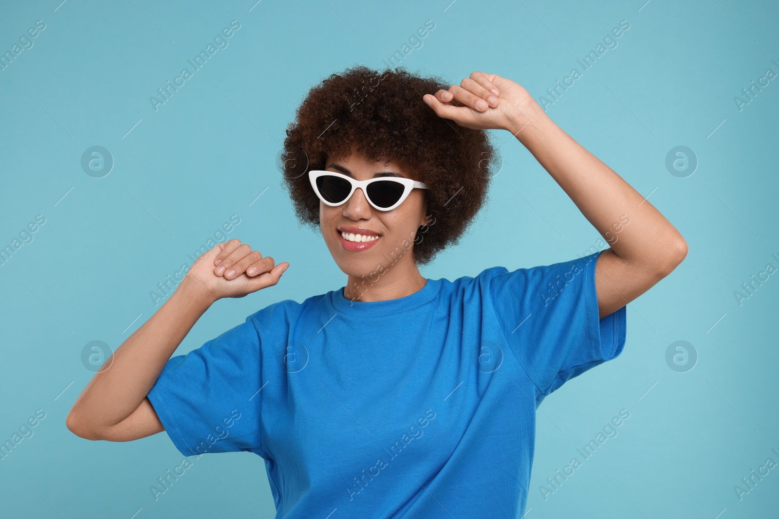 Photo of Happy young woman in stylish sunglasses dancing on light blue background