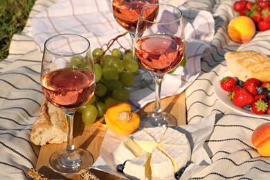 Glasses of delicious rose wine and food on white picnic blanket outdoors
