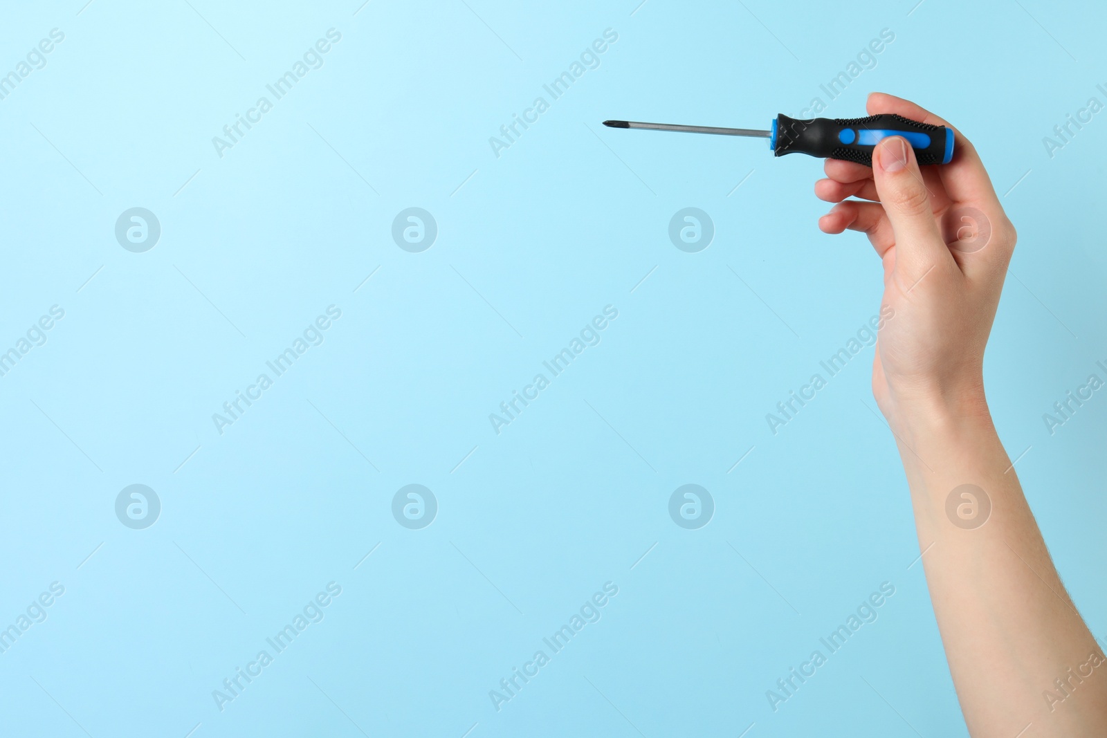 Photo of Woman holding screwdriver on light blue background, closeup. Space for text