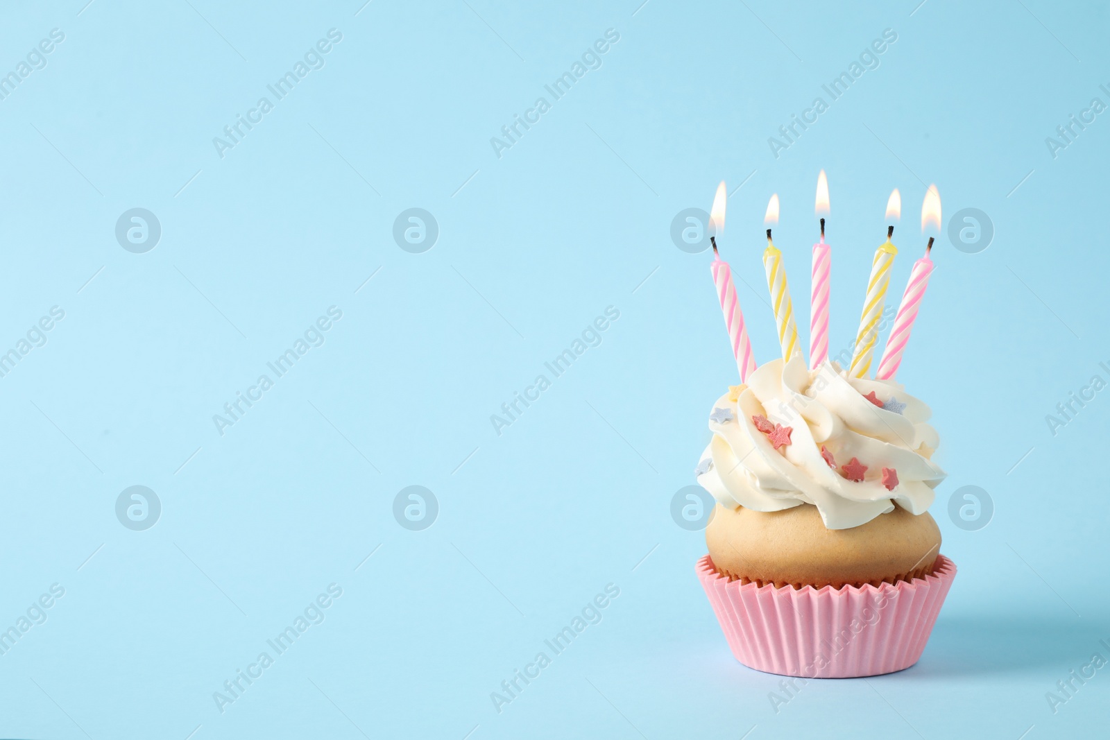 Photo of Birthday cupcake with candles on light blue background. Space for text