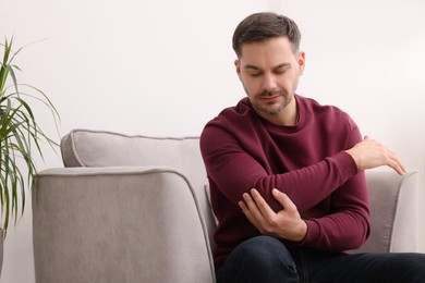 Photo of Man suffering from pain in his elbow on armchair indoors