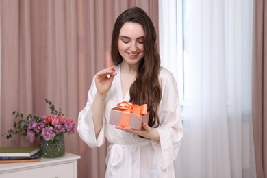 Photo of Beautiful happy young woman holding gift box in room