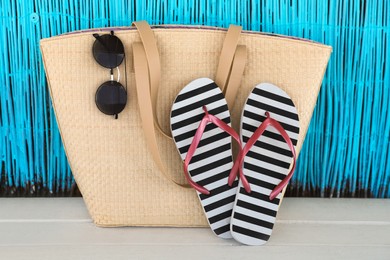 Photo of Stylish flip flops, bag and sunglasses on white wooden table