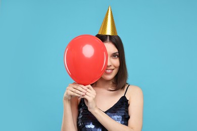 Photo of Happy young woman in party hat with balloon on light blue background