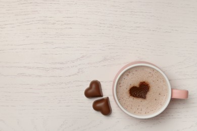 Photo of Cup of aromatic coffee with heart shaped decoration and chocolate candies on white wooden table, top view. Space for text