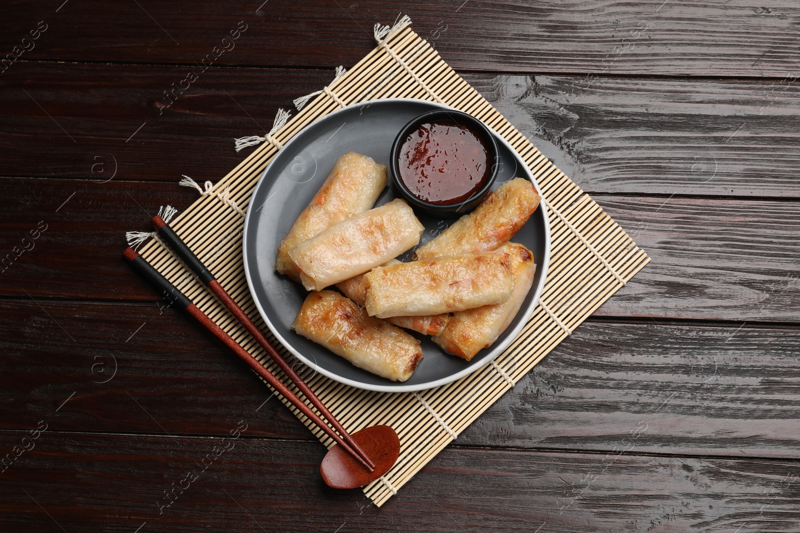 Photo of Tasty fried spring rolls and sauce served on wooden table, top view