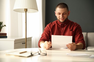 Photo of Man reading paper letter at white table in room