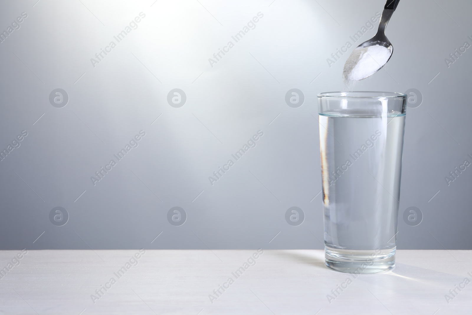 Photo of Adding baking soda into glass of water at white table against light grey background. Space for text