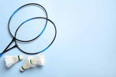 Photo of Feather badminton shuttlecocks and rackets on light blue background, flat lay. Space for text