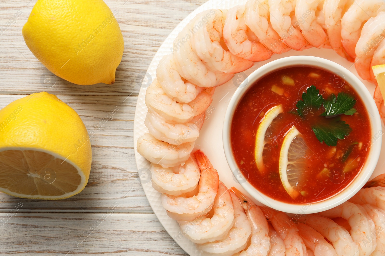 Photo of Tasty boiled shrimps with cocktail sauce and lemon on white wooden table, top view