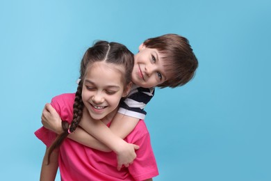 Happy brother and sister hugging on light blue background