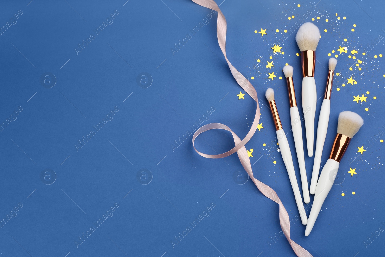 Photo of Different makeup brushes, ribbon and shiny confetti on blue background, flat lay. Space for text