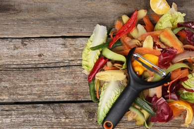 Photo of Peels of fresh vegetables and peeler on wooden table, top view. Space for text