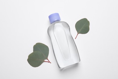 Photo of Bottle of baby oil and eucalyptus leaves on white background, flat lay