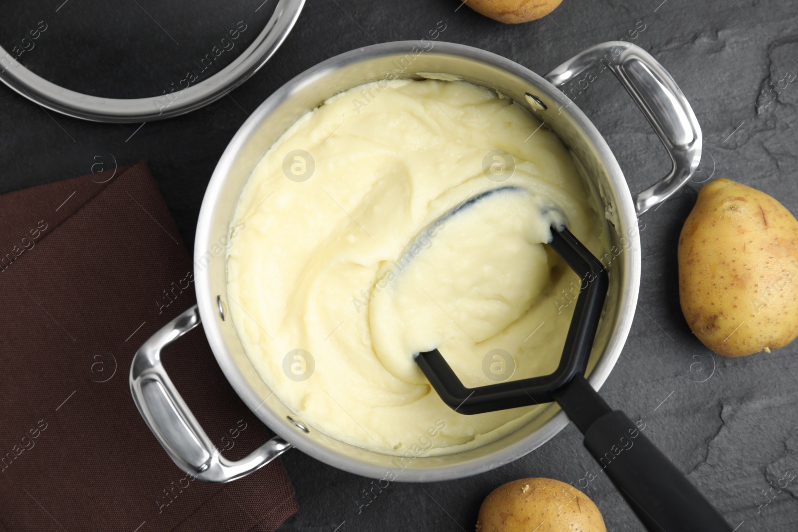 Photo of Pot of freshly cooked homemade mashed potatoes and raw vegetables on black table, flat lay