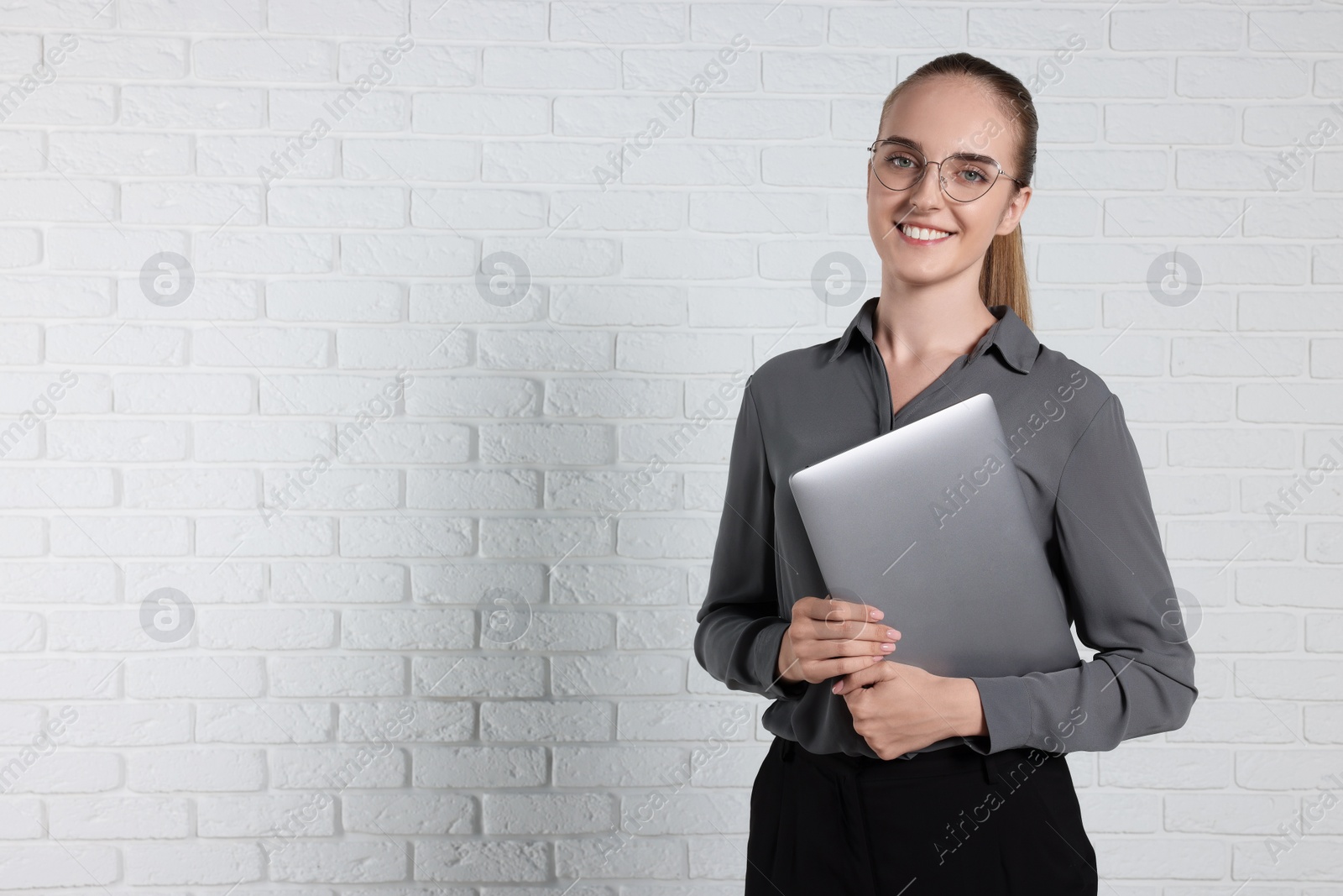 Photo of Happy young secretary with laptop near white brick wall, space for text