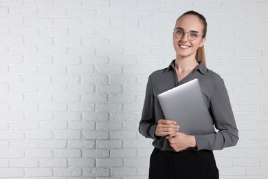 Photo of Happy young secretary with laptop near white brick wall, space for text