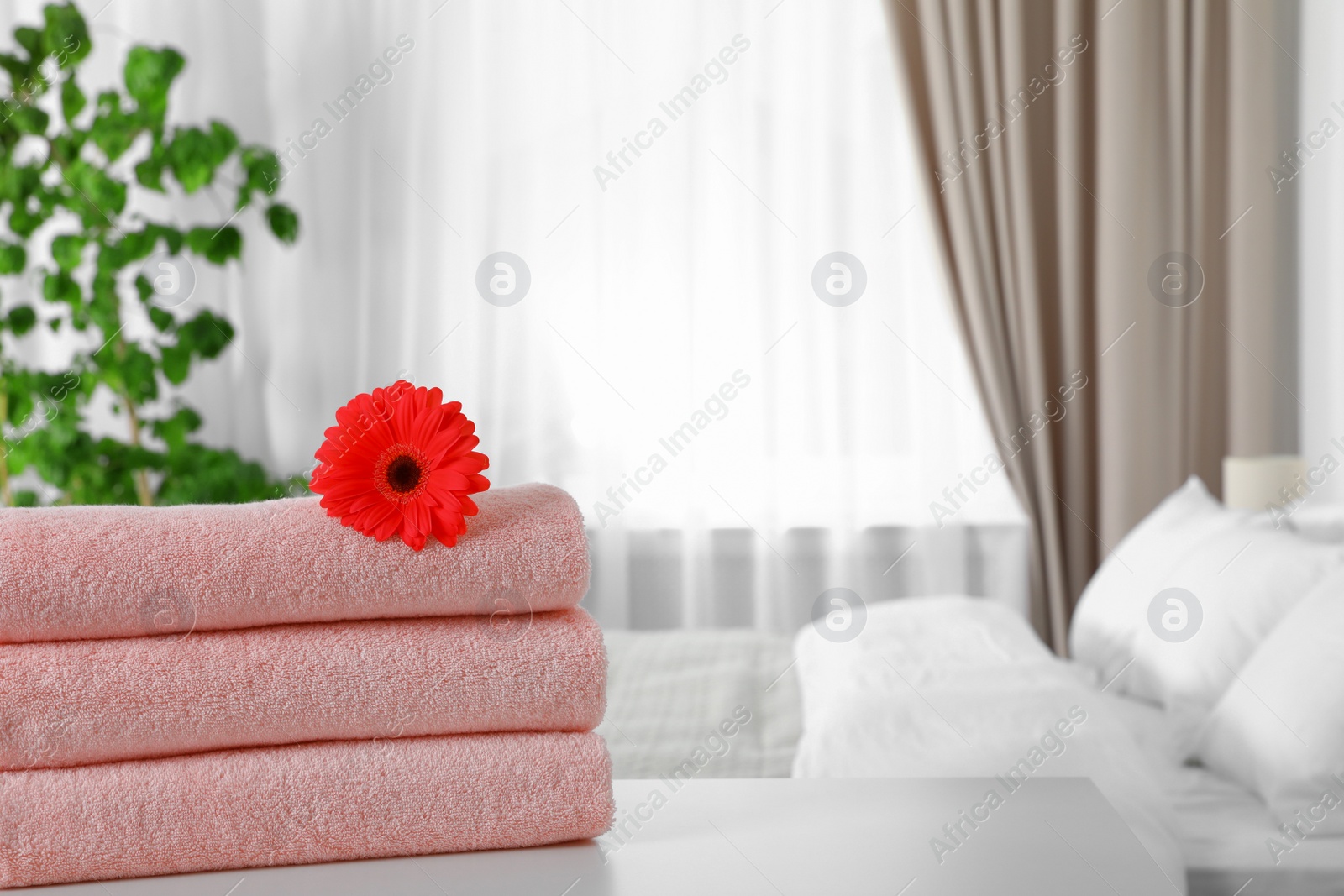 Photo of Stack of fresh towels with flower on table in bedroom. Space for text