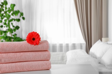 Photo of Stack of fresh towels with flower on table in bedroom. Space for text