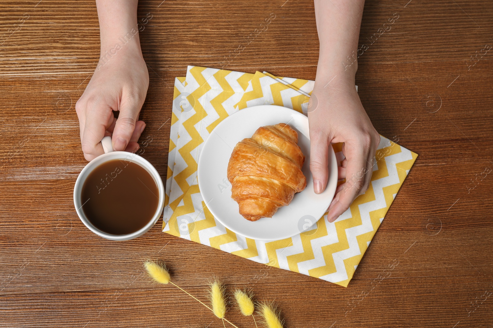 Photo of Young woman having breakfast with tasty croissant and cup of coffee at table, top view