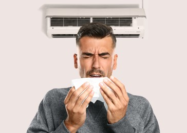 Image of Man suffering from cold in room with air conditioner on white wall
