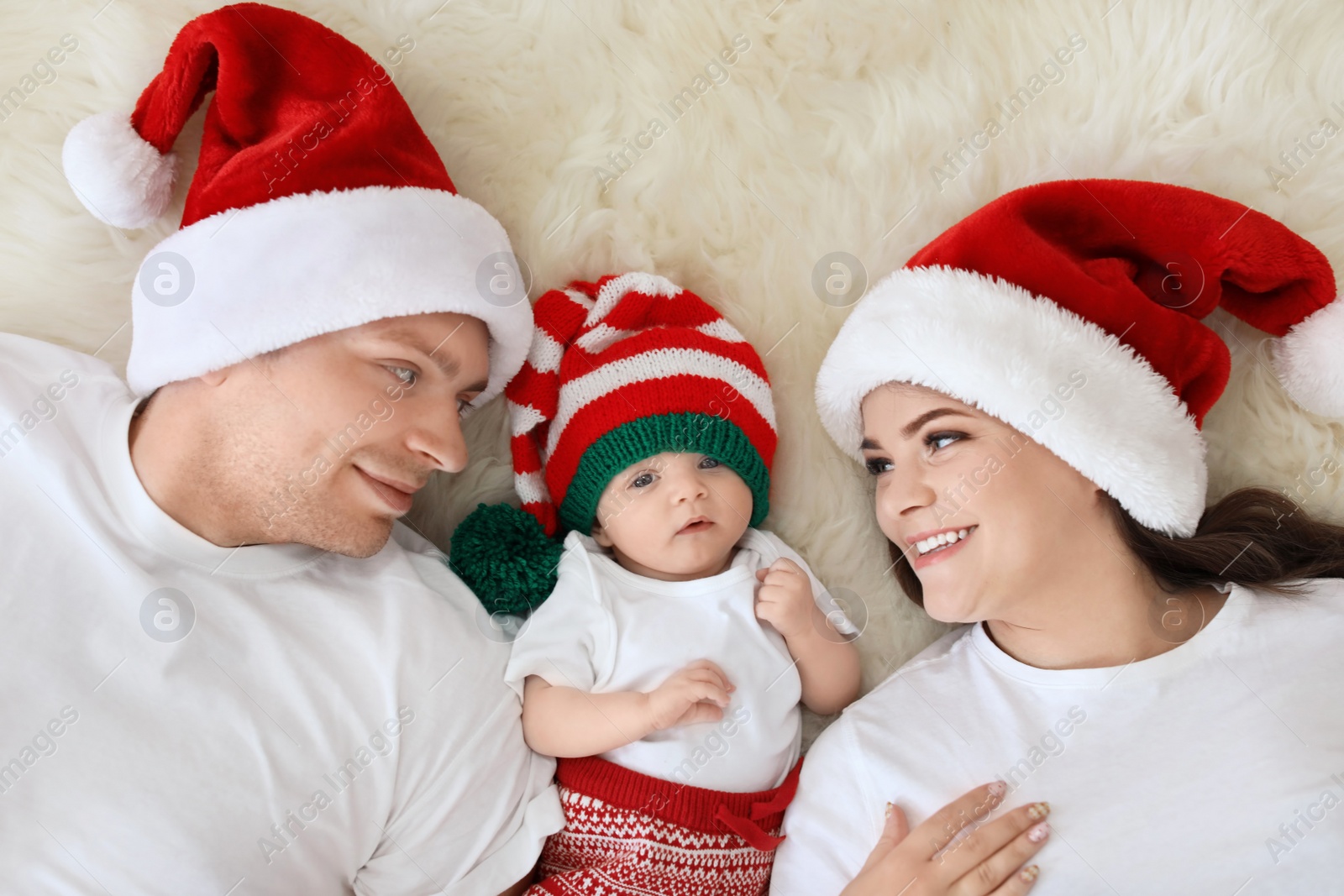 Photo of Happy couple with baby in Christmas hats on fuzzy rug, top view