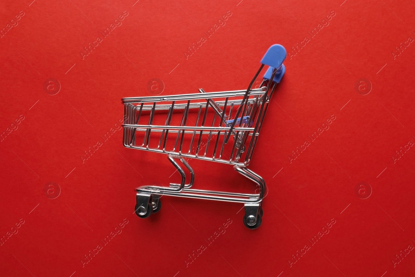 Photo of Small metal shopping cart on red background, top view