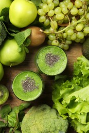 Glasses of fresh green smoothie and ingredients on wooden table, flat lay