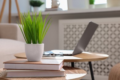 Photo of Potted artificial plant, laptop and books on wooden nesting tables indoors